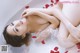 A woman laying in a bathtub with rose petals on the floor.