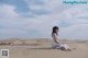 A woman in a white dress sitting on a sand dune.